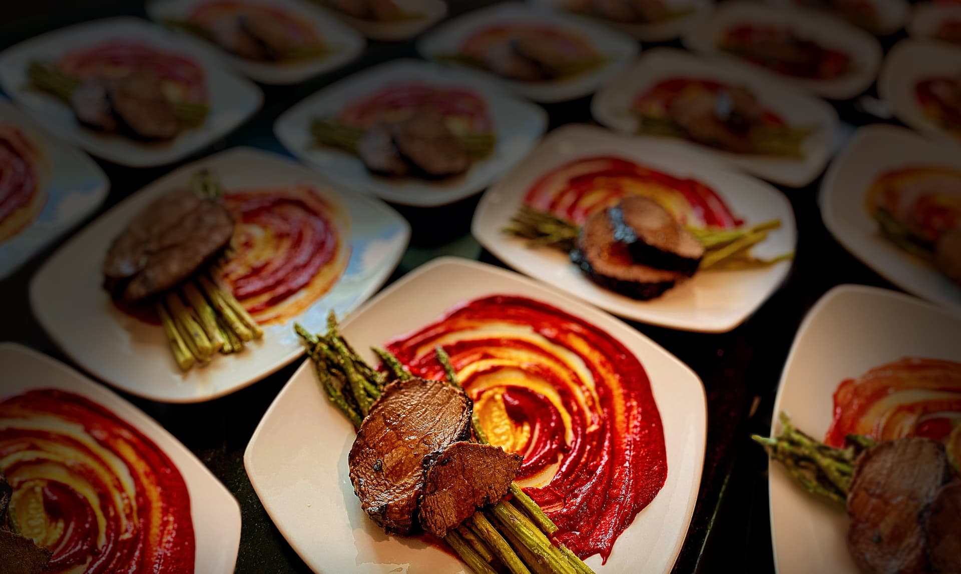 Plated courses with seared meat, asparagus, and a red pepper reduction